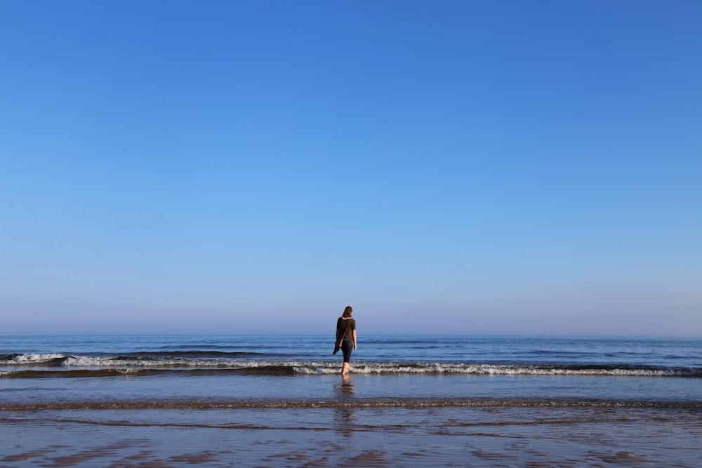 woman in black dress walking on beach during daytime