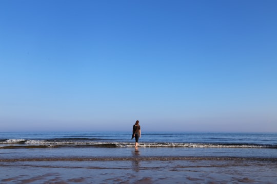 woman in black dress walking on beach during daytime in Three Cliff Bay United Kingdom