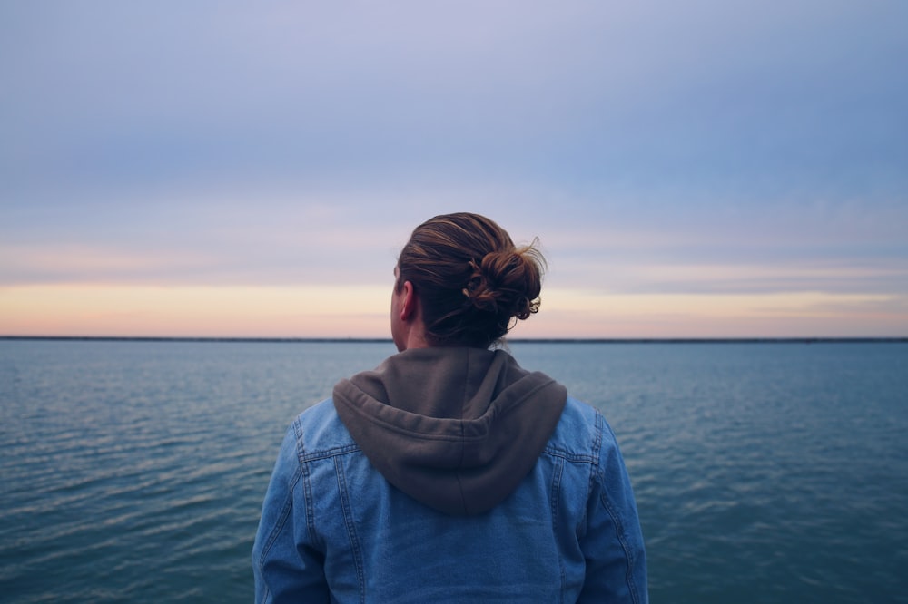 Femme en veste en jean bleue debout près d’un plan d’eau pendant la journée