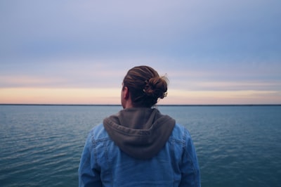woman in blue denim jacket standing near body of water during daytime thoughtful google meet background