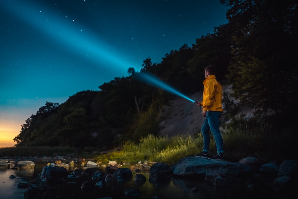 man holding flashlight standing on gray stone during nighttime