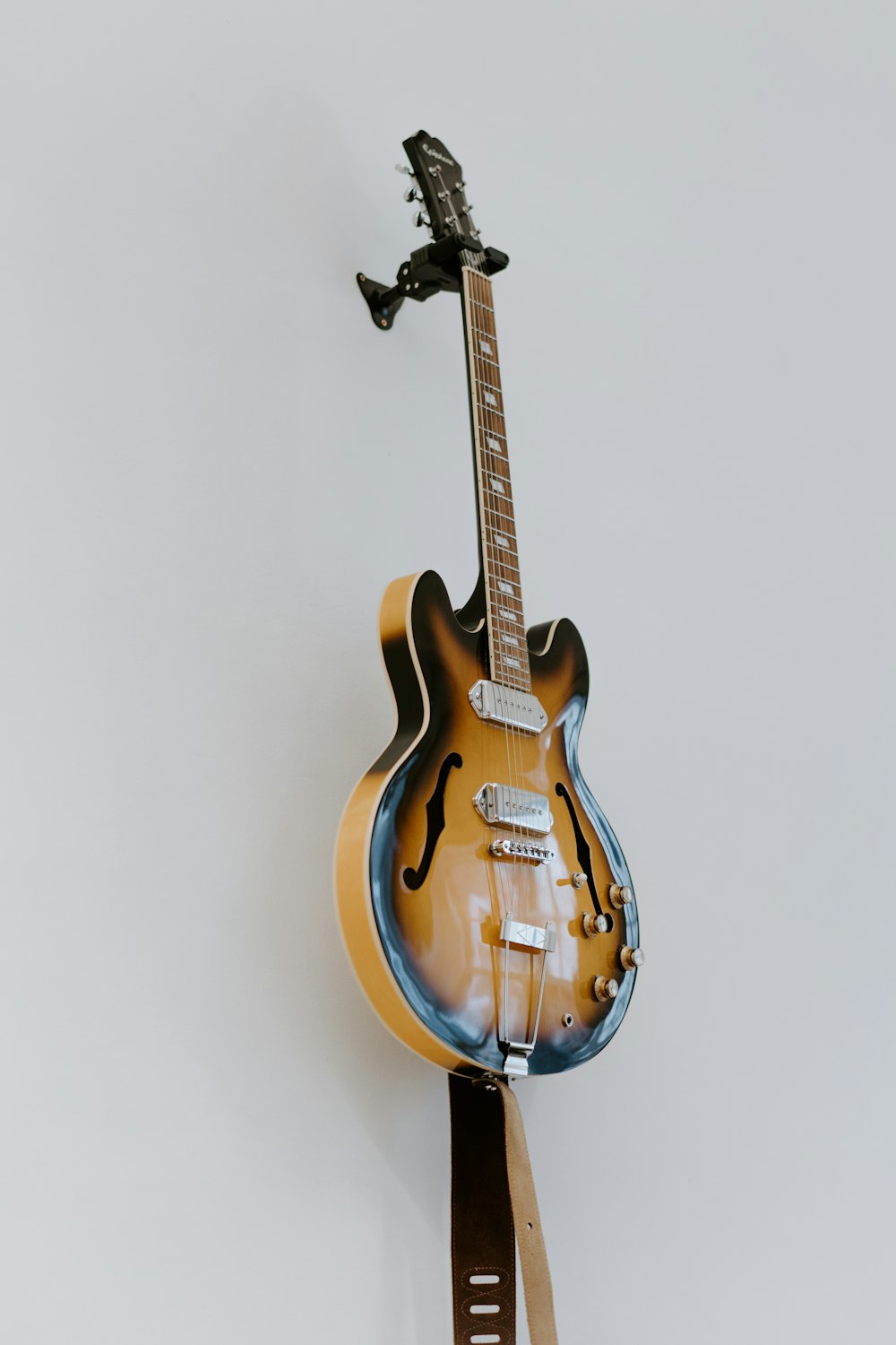 brown electric guitar beside white wall