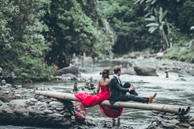 couple sitting on tree while looking for body of water at daytime