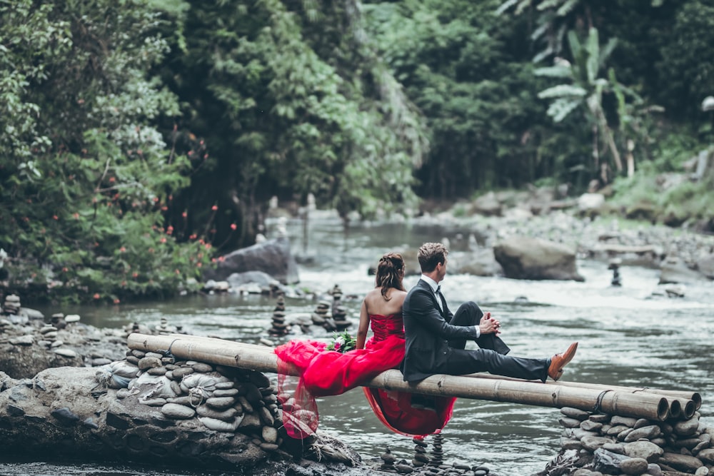 couple sitting on tree while looking for body of water at daytime