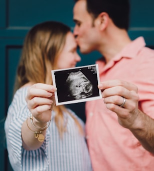 man kissing woman's forehead white holding ultrasound photo