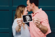man kissing woman's forehead white holding ultrasound photo