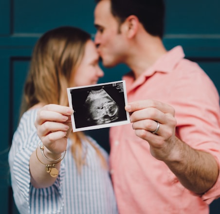 man kissing woman's forehead white holding ultrasound photo