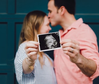 man kissing woman's forehead white holding ultrasound photo