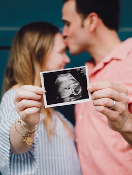 man kissing woman's forehead white holding ultrasound photo