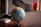 A terrestrial globe is positioned on a wooden table, with a few books stacked nearby. The globe displays detailed world geography with various countries and continents visible. In the background, there is a blurred image of a window with a red curtain or object partially visible.