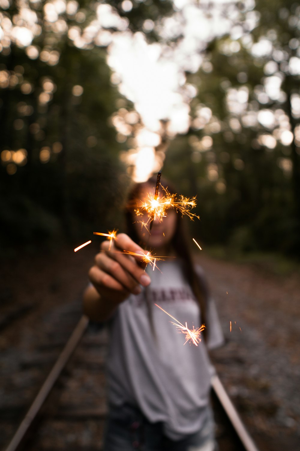 woman holding firecracker standing on train rail surround by trees