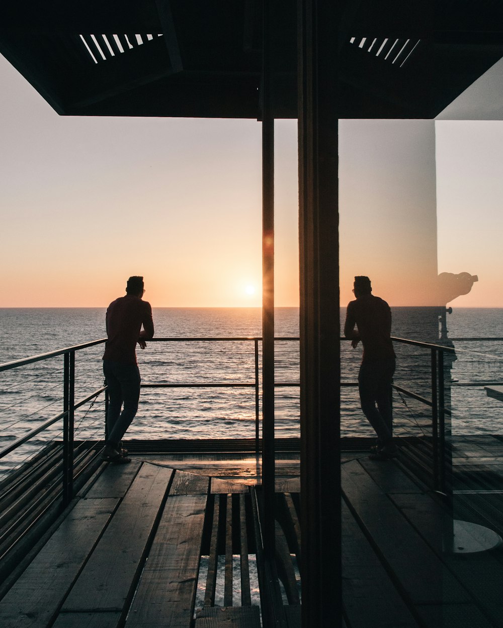 silhouette of man standing on gray stainless steel railing looking at sunset