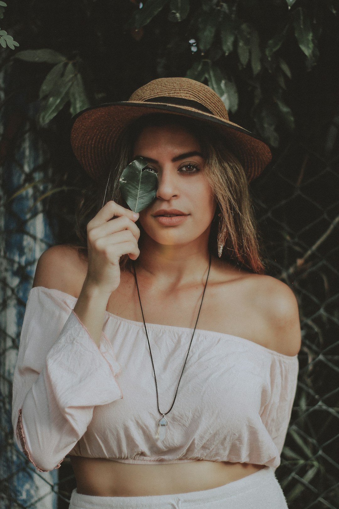 selective focus photography of women in off-shoulder long-sleeved crop shirt holding leaf covering her one eye