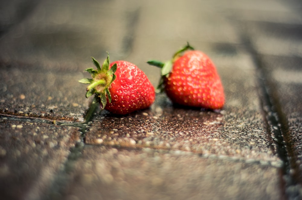 tilt-shift photography of two strawberries on gray brick pavement