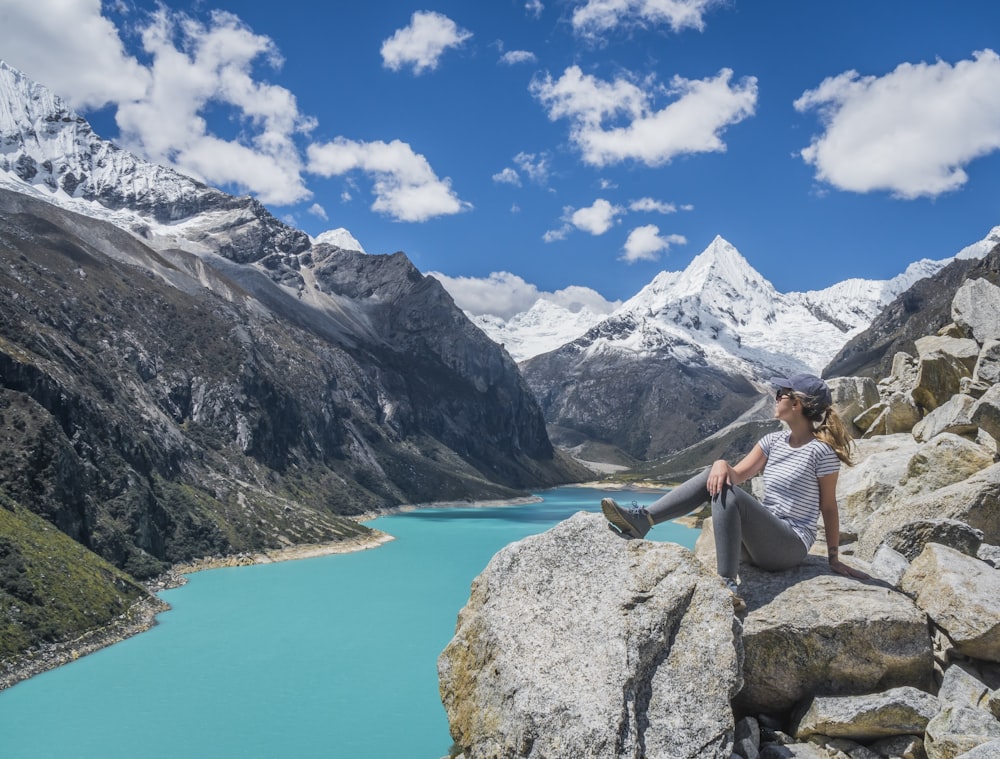 girl sitting on rock near body of water at daytime