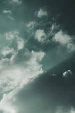 Cloud formations against a muted greenish sky, with a mix of fluffy and wispy textures creating a sense of movement.