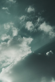 Cloud formations against a muted greenish sky, with a mix of fluffy and wispy textures creating a sense of movement.