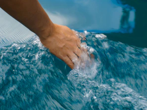 Close-up of hands gently touching water, reflecting calming shades of blue and sand