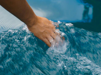 Close-up of hands gently touching water, reflecting calming shades of blue and sand