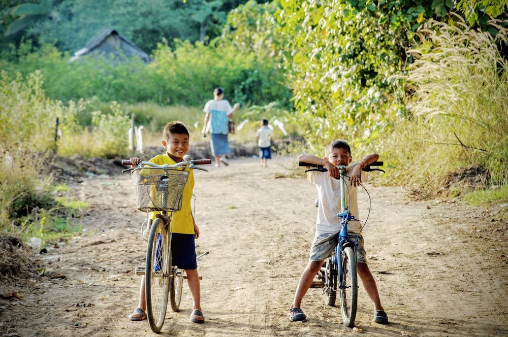 two boy riding on bicycle on dirt road