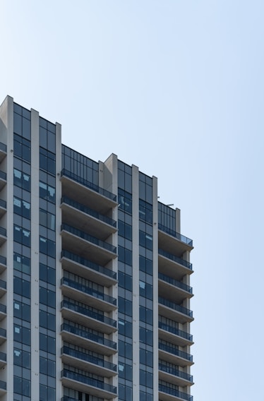 Close-up of a modern residential tower with clean lines and glass balconies under a clear sky.