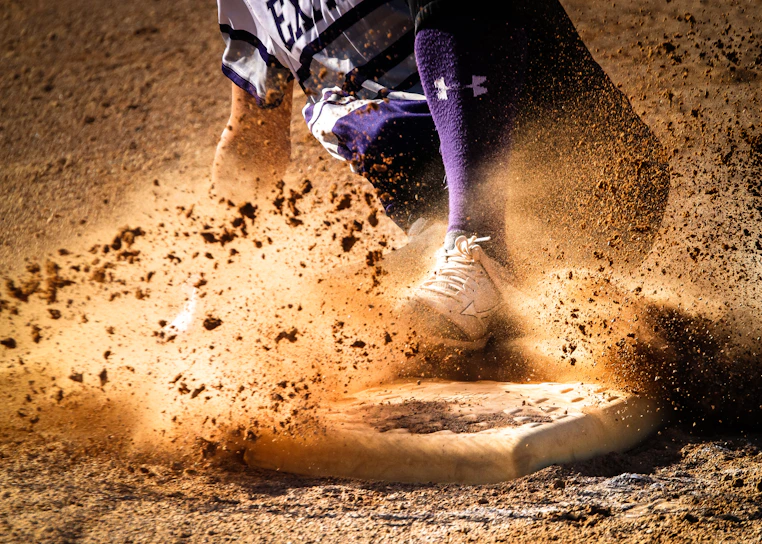 A close-up action shot of a softball player sliding into base with dust flying around.