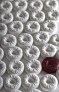 A collection of circular mint candies, predominantly white, with one standout candy in red. Each candy is embossed with the word 'LIFE SAVERS'.