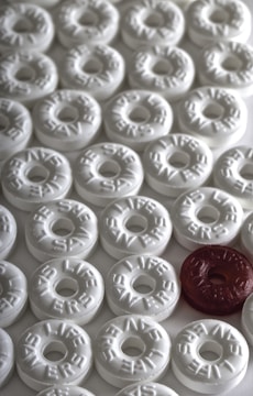 A collection of circular mint candies, predominantly white, with one standout candy in red. Each candy is embossed with the word 'LIFE SAVERS'.