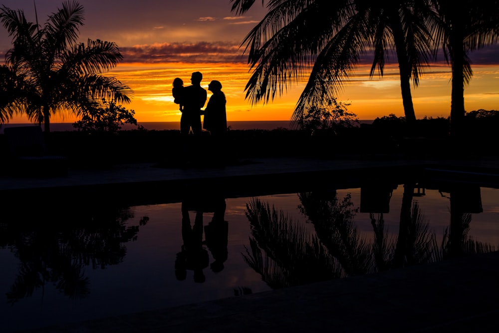 silhouette photo of three person near body of water during sunset