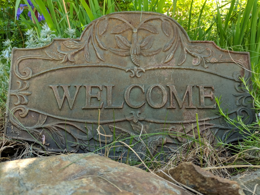 A charming outdoor welcome sign hanging on a rustic wooden door surrounded by greenery.