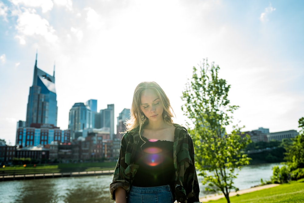 woman wearing gray and black long-sleeved shirt standing on grass field near river during daytime