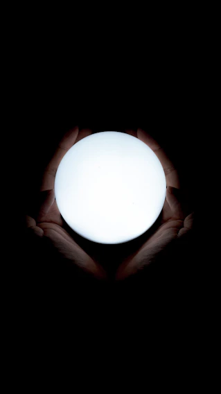 Soft lavender-hued hands gently holding a glowing orb of light symbolizing healing energy.