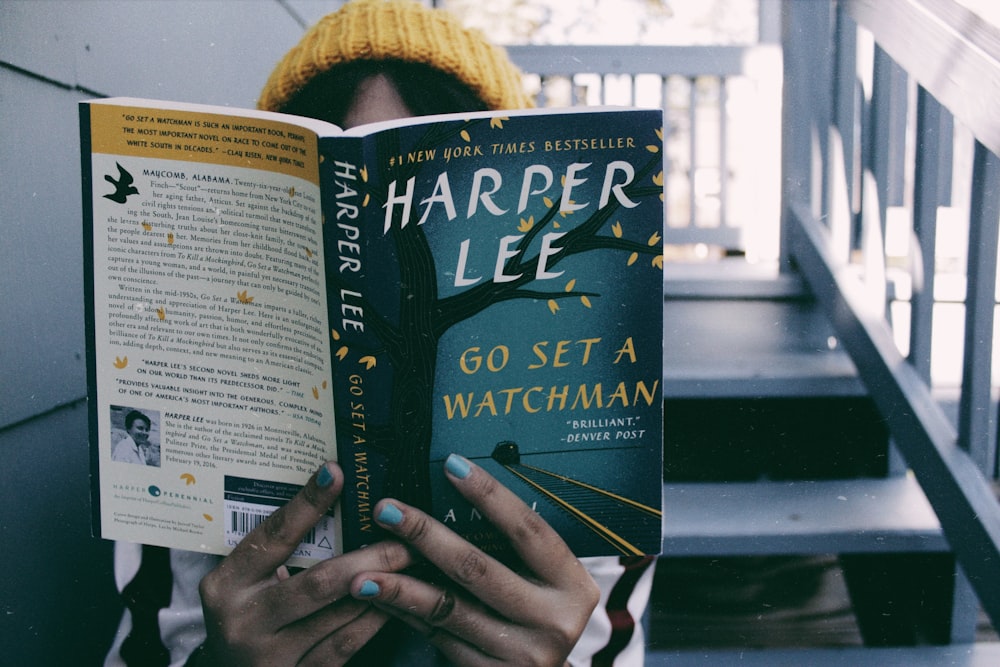 person sitting on stairs while reading Harper Lee book