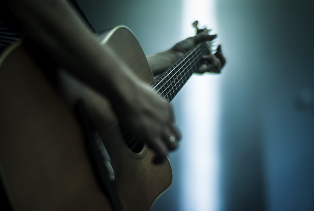 person playing acoustic guitar shallow focus photography