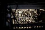 A rack of audio or sound equipment with various cables, connectors, and input panels. The focus is on multiple connection ports and electrical components, organized in a compact space under dim lighting. The equipment includes labels and small indicator lights.
