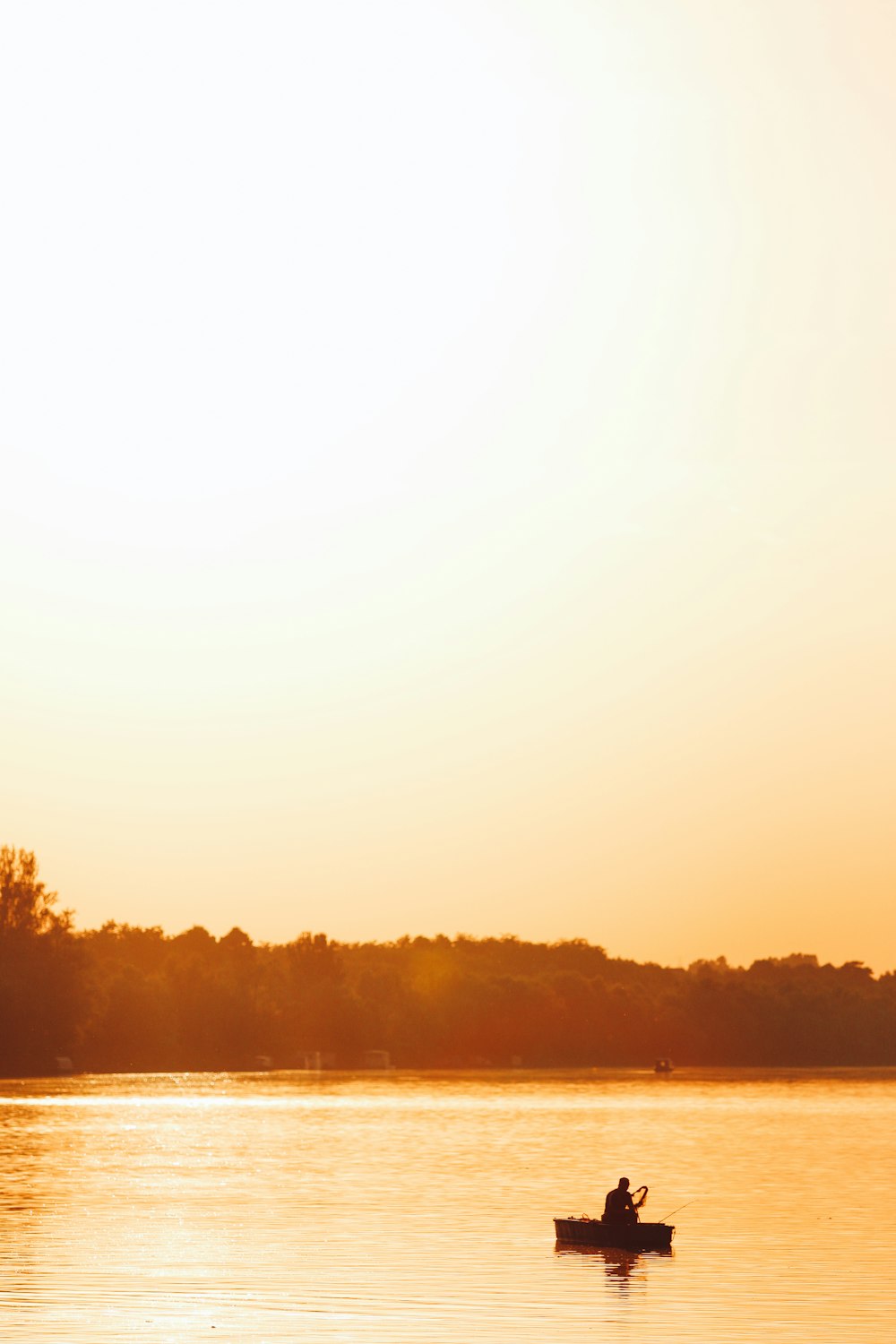 silhouette of person on boat at the center of the lake under clear sky