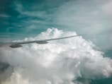 A close-up of a plane wing cutting through fluffy white clouds.