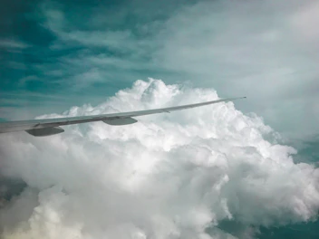 Close-up shot of a sleek airplane wing cutting through bright blue sky dotted with fluffy clouds.
