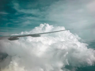 Close-up shot of a sleek airplane wing cutting through bright blue sky dotted with fluffy clouds.
