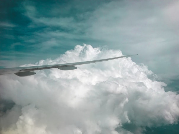 An aerial view of fluffy clouds with a plane wing cutting through the blue sky.