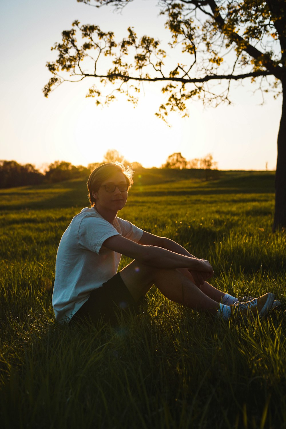 man sitting on grass while resting hand on knee during golden hour