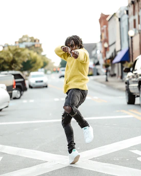 Casual styling shot of sway bound jeans paired with a lightweight yellow-sleeved pullover on a city street bench