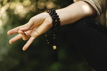 Hands holding traditional yoga mala beads over a serene outdoor background.