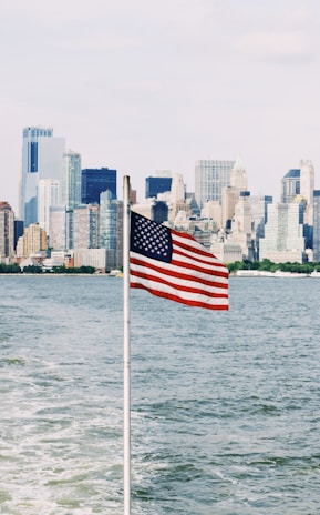 The American flag waving gently with a city skyline in the background during golden hour.