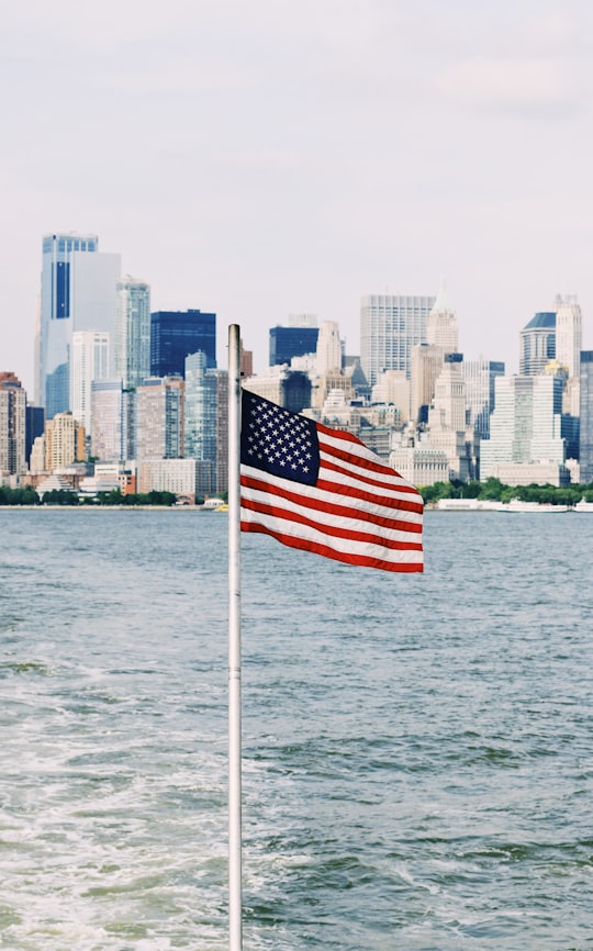 U.S.A. flag on pole near sea under cloudy sky in New York City United States
