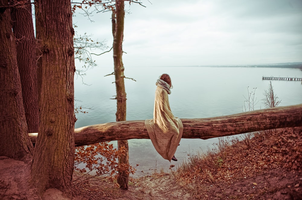 woman sitting on tree log facing at body of water