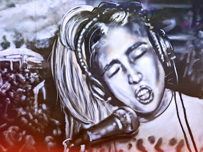 A black and white mural depicts a person with closed eyes singing passionately into a microphone. The person wears headphones and has light-colored hair. The background includes a crowd of people, suggesting a concert or performance setting. The image is artistically stylized, creating a dramatic and energetic atmosphere.