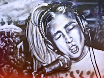 A black and white mural depicts a person with closed eyes singing passionately into a microphone. The person wears headphones and has light-colored hair. The background includes a crowd of people, suggesting a concert or performance setting. The image is artistically stylized, creating a dramatic and energetic atmosphere.