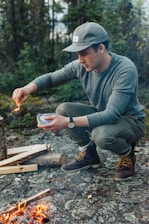 A person practicing fire-starting techniques outdoors with survival gear.