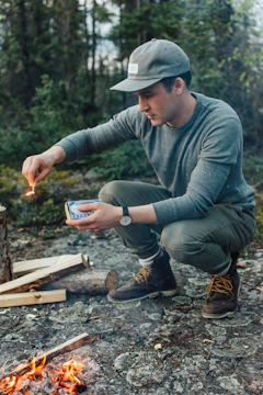 A person demonstrating fire-starting techniques in a forest setting.
